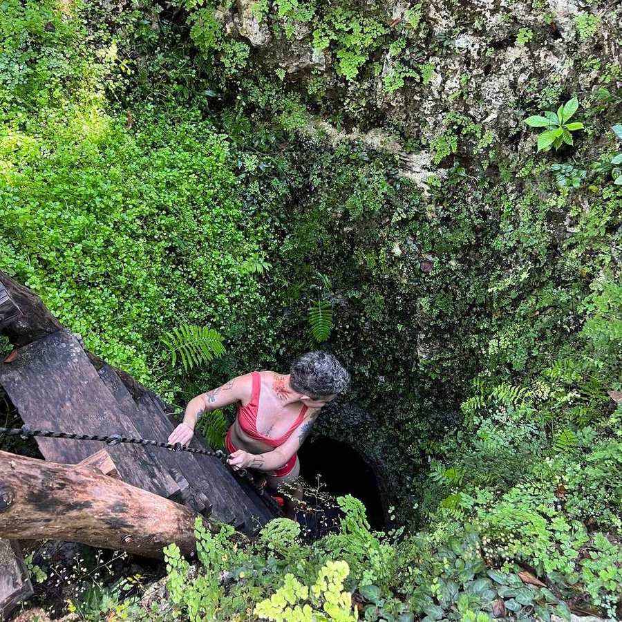 Guide descending a wooden ladder into a secret cenote in the jungle, Tulum